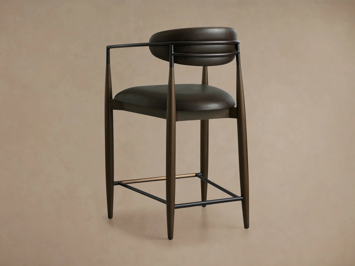 Jagger Faux Leather Stool featuring a dark brown faux leather seat and backrest with a curved design, supported by sleek dark metal and tapered wooden legs.