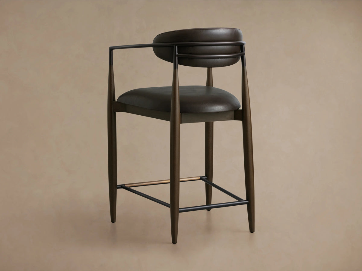 Dark brown Jagger Faux Leather Stool with curved backrest, faux leather upholstery, and metal accents over wooden legs.