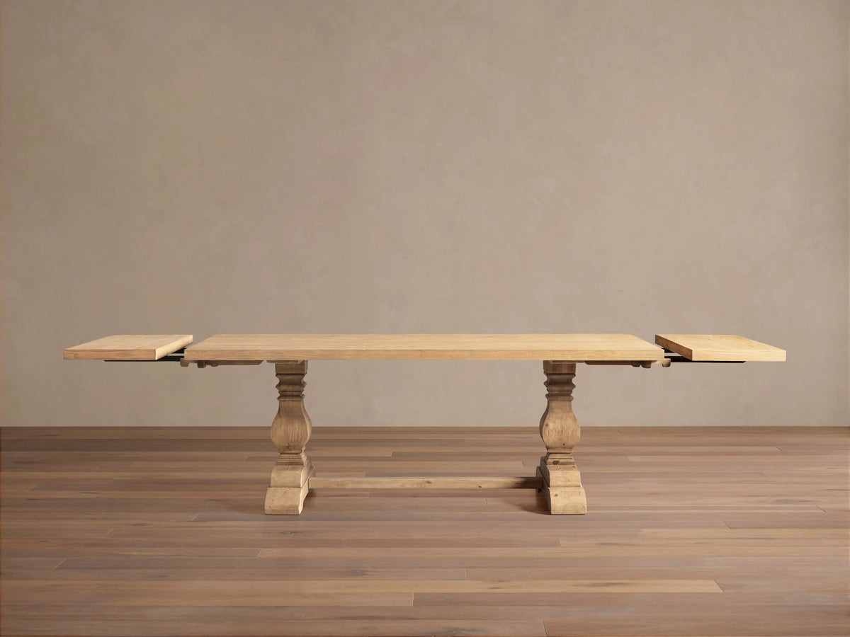 Kensington Dining Table: Long, light natural oak table with two carved pedestal bases & leaf extensions, on wood floor.