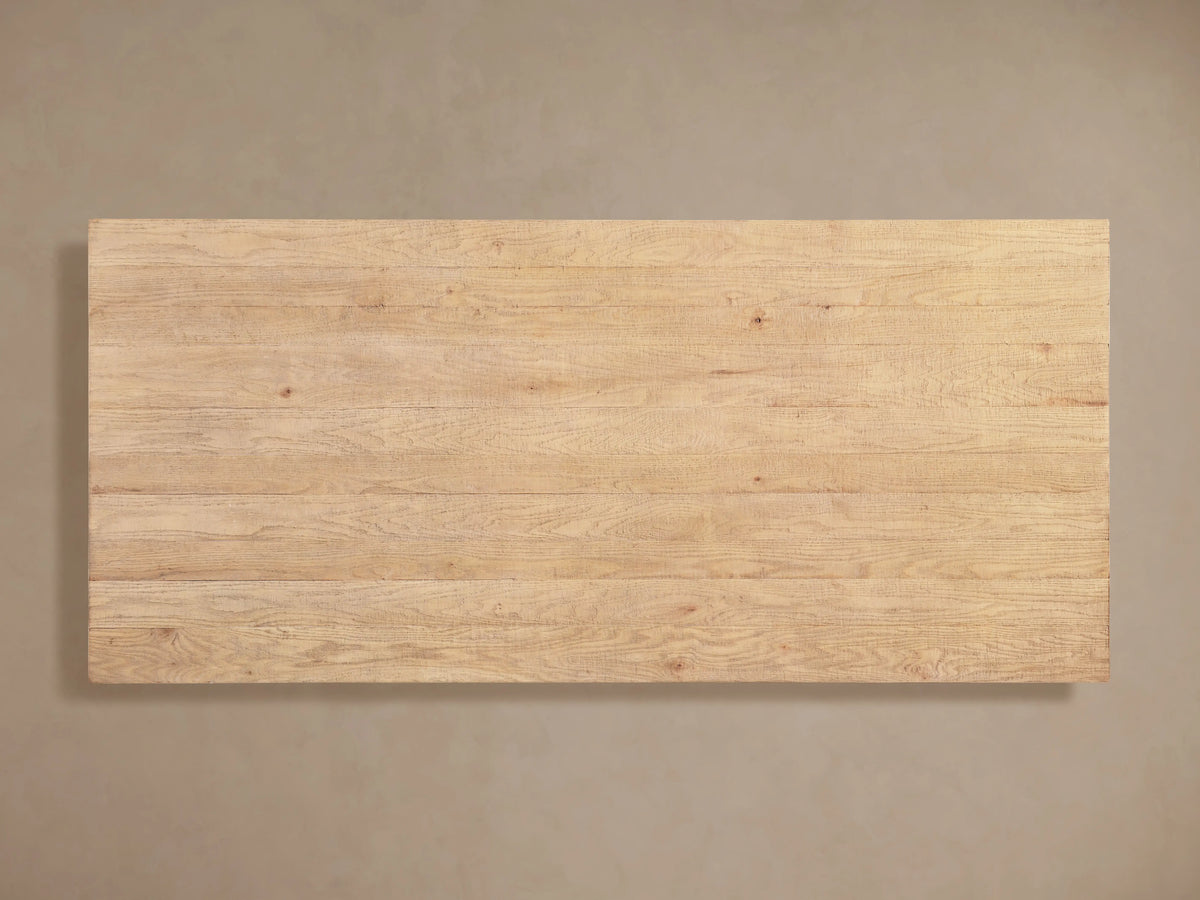 Angled close-up of Kensington Dining Table's light oak plank top with distinct wood grain, texture. Part of a carved base.