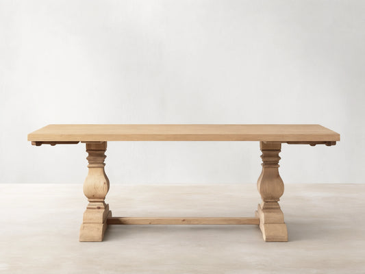Light natural wood Kensington Dining Table, rectangular top, two chunky carved pedestal bases, shown straight on a wood floor.