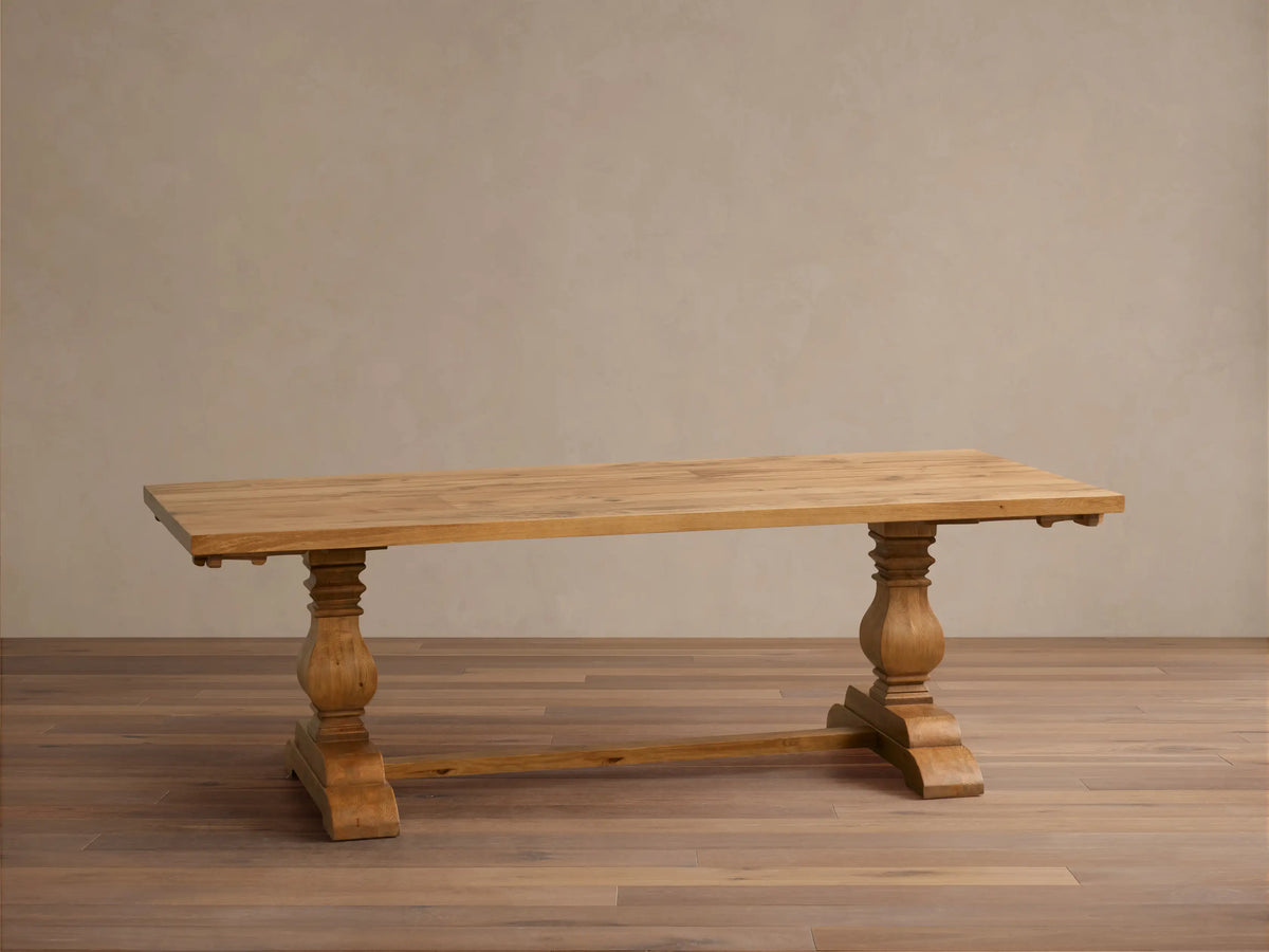 Kensington Reclaimed Dining Table, light brown, rectangular, with two carved pedestal bases, on a wood floor against a beige wall.