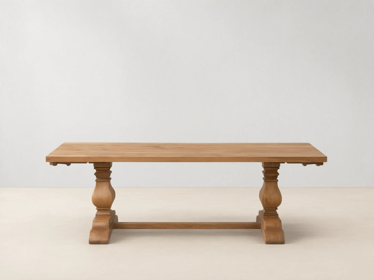 Kensington Reclaimed Dining Table with a light wood rectangular top, supported by two ornate turned pedestal bases, on a wood floor.