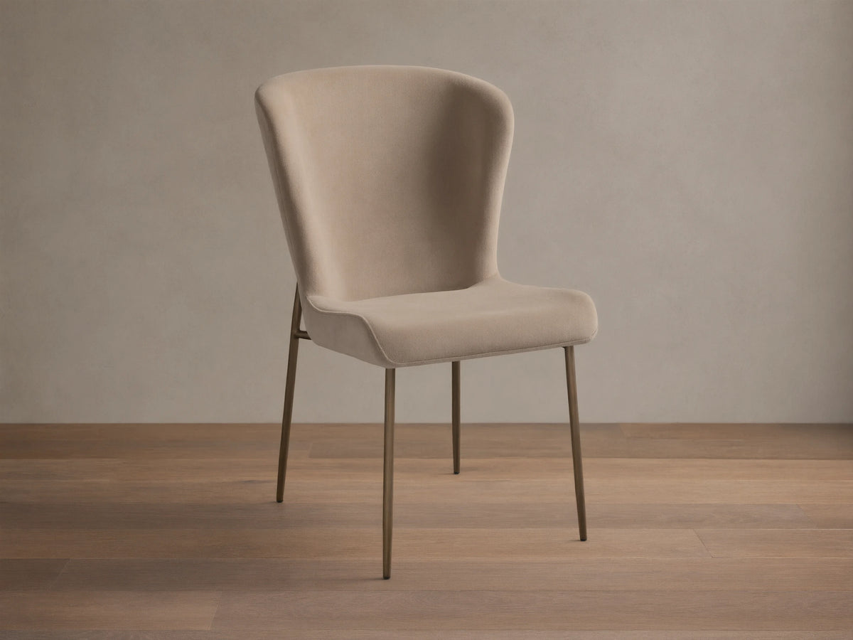 Kirsten High Back Dining Chair, upholstered in light beige, featuring a curved high back and slim metallic bronze legs, angled.