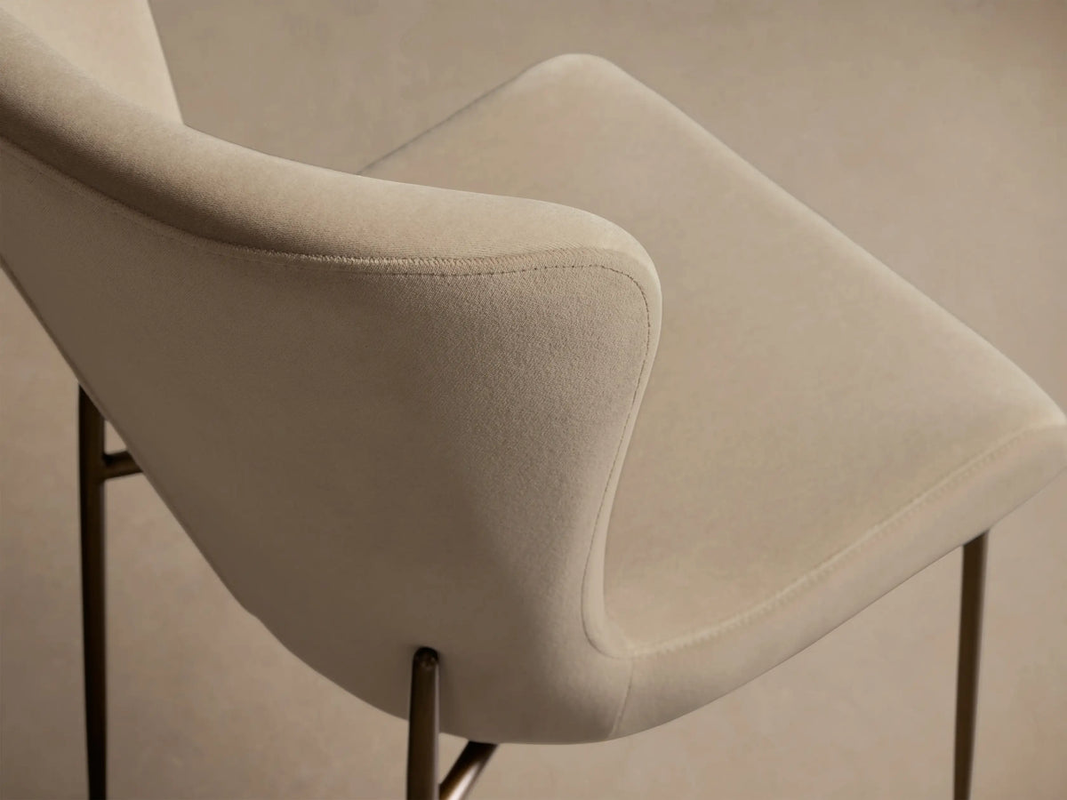Kirsten High Back Dining Chair: Beige upholstered, curved high back, four thin gold metal legs, on a wooden floor.