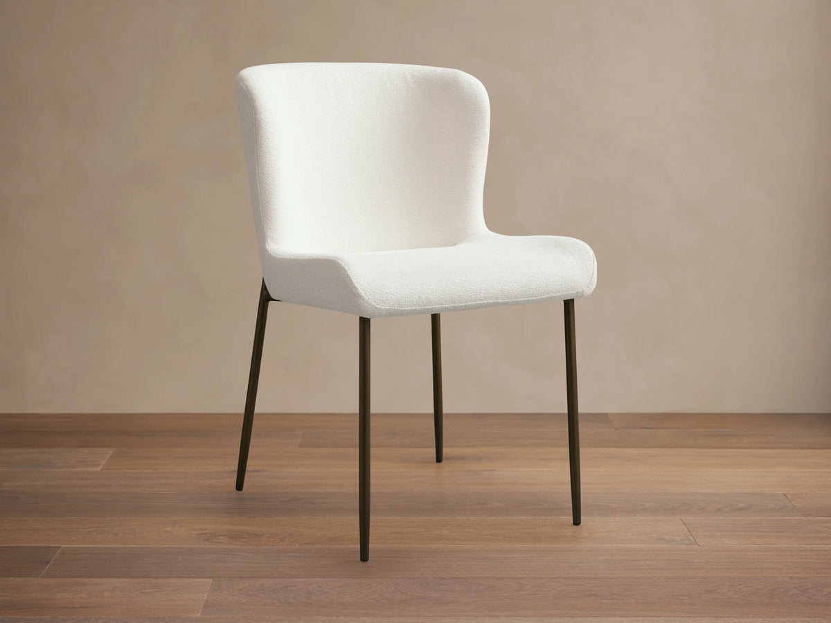 Kirsten Dining Chair with white upholstered seat and backrest, featuring slim black iron legs on a wooden floor.