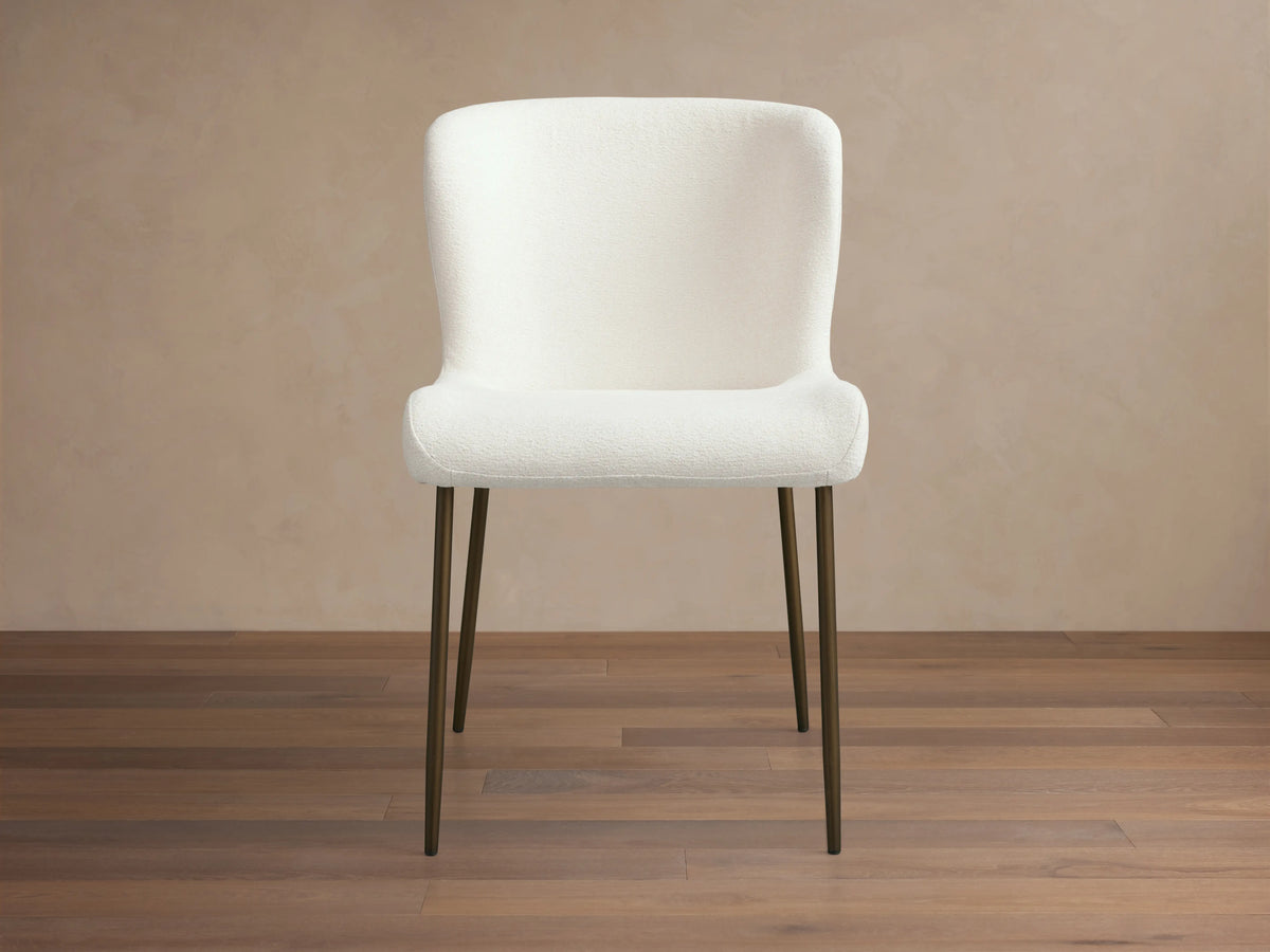 Kirsten Dining Chair with a white upholstered seat and backrest on slim, black iron legs, set against a wooden floor and neutral wall.