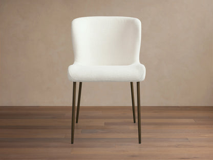 Kirsten Dining Chair with a white upholstered seat and backrest on slim, black iron legs, set against a wooden floor and neutral wall.