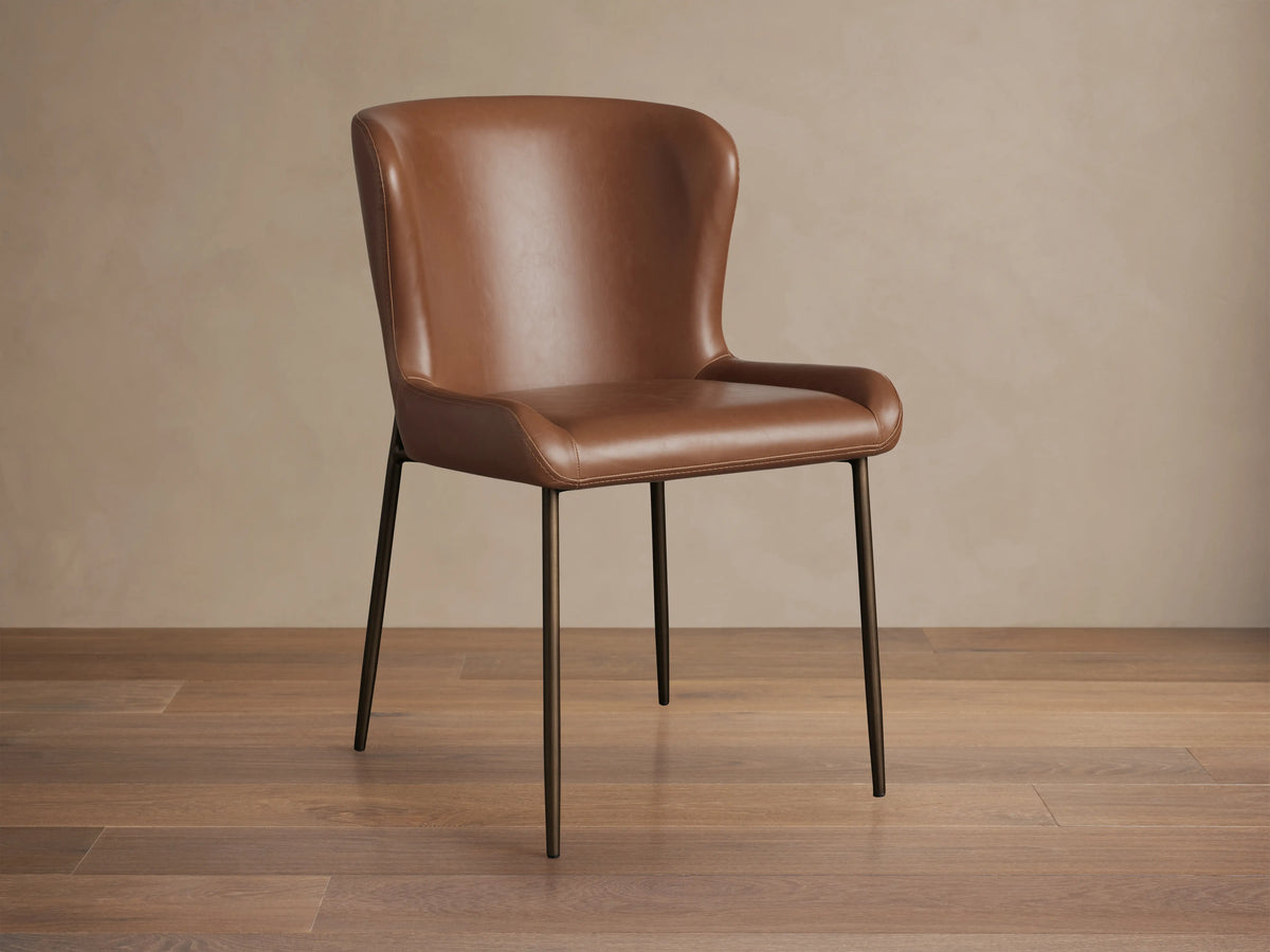Kirsten Faux Leather Dining Chair with brown faux leather upholstery, curved backrest, and sleek black powder-coated iron legs.