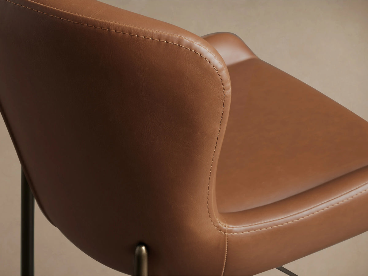 Kirsten Faux Leather Dining Chair with smooth brown faux leather upholstery, visible stitching, and black iron legs in close-up view.