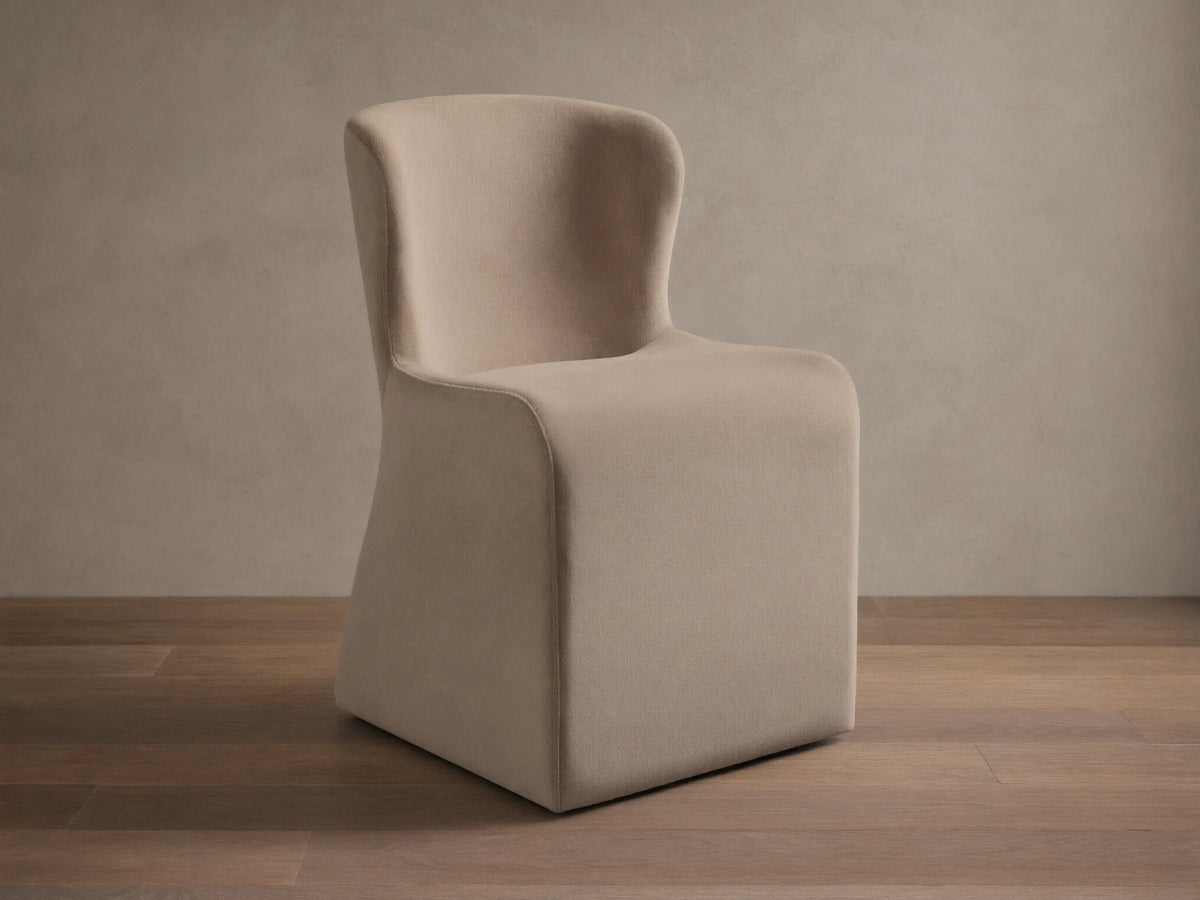 Kirsten Upholstered Dining Chair, beige, with a curved back and solid block base, on a wooden floor.