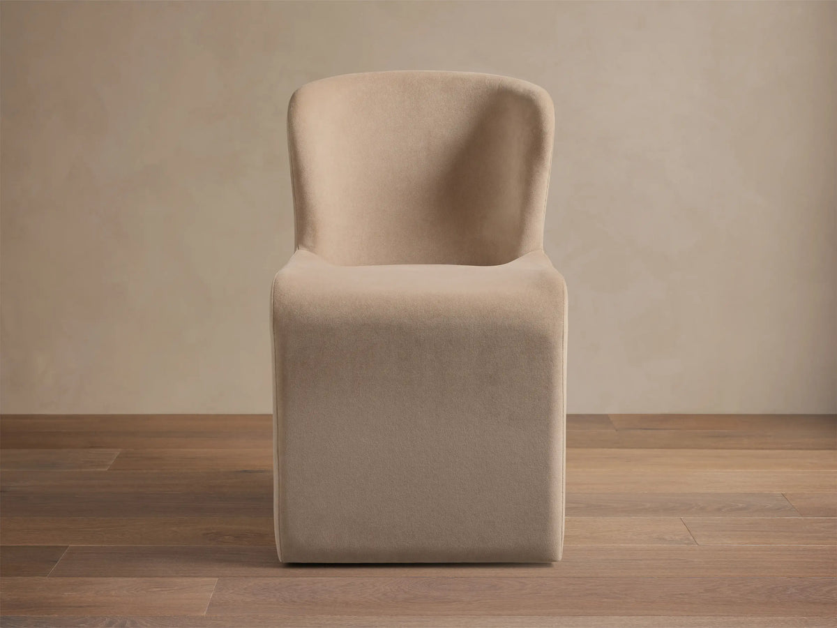 Kirsten Upholstered Dining Chair, beige, with a curved back and solid block base, on a wooden floor.