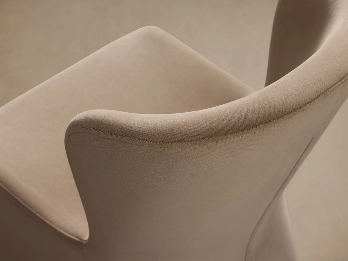 Kirsten Upholstered Dining Chair, beige, facing front. Curved back, solid base on wooden floor against a light wall.