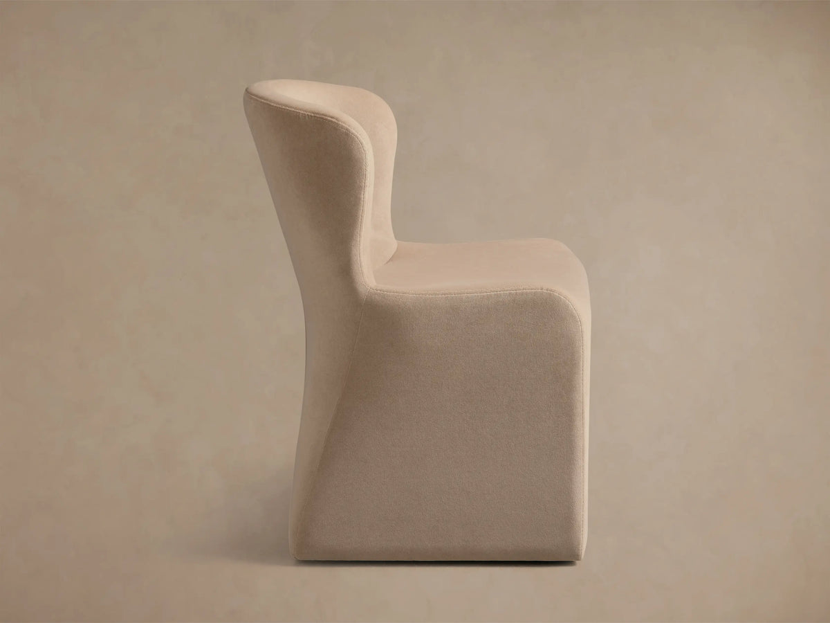 Kirsten Upholstered Dining Chair, light beige, angled back view with gracefully curved backrest and subtle vertical seam.