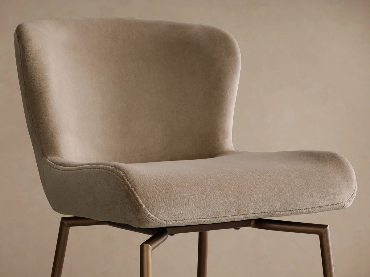 Front view of a beige Kirsten Swivel Stool with an upholstered seat and back, and a matte bronze slender iron frame with footrests.