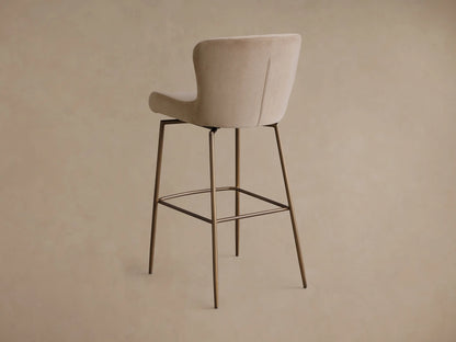 Close-up of the beige Kirsten Swivel Stool showing its curved upholstered seat and backrest with brown metal frame.