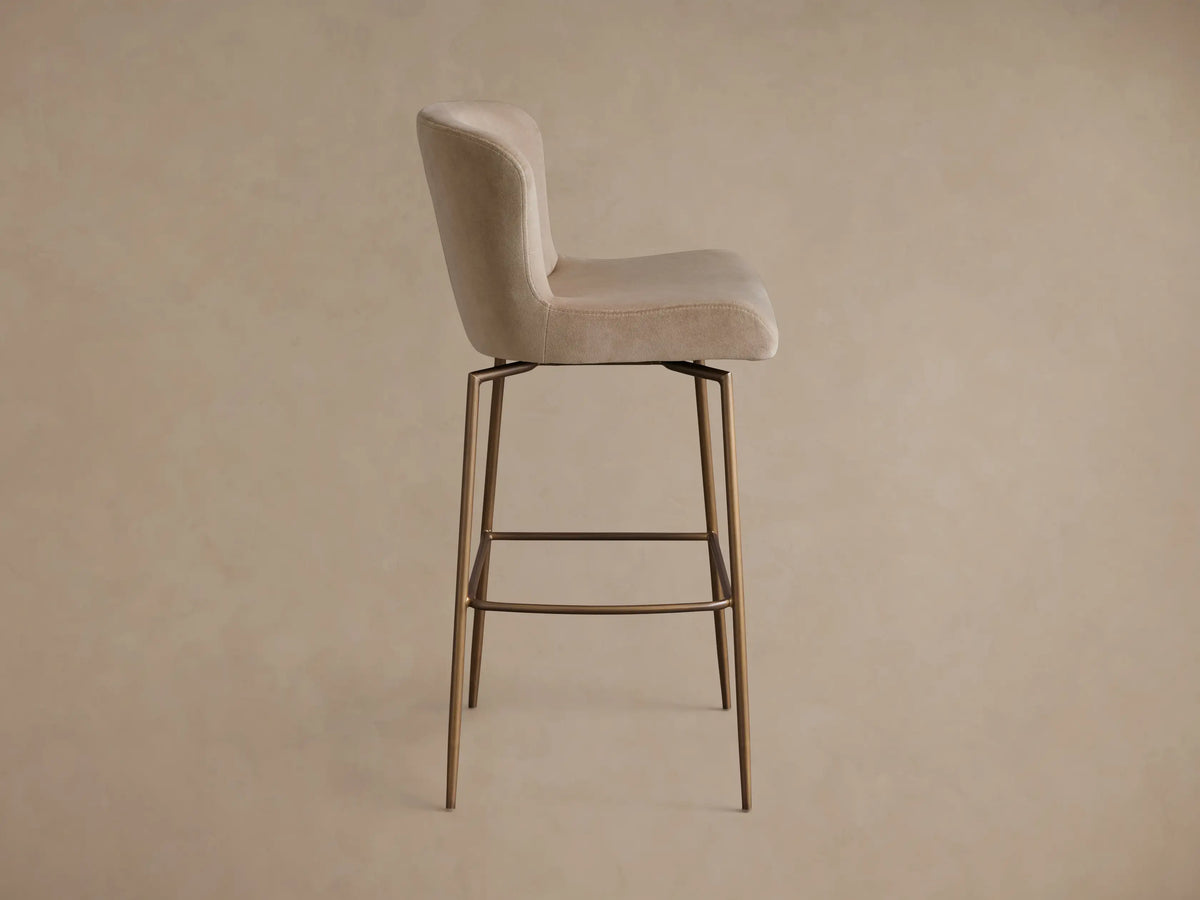 Front view of a beige velvet Kirsten Swivel Stool with a curved back and dark bronze powder-coated metal legs.