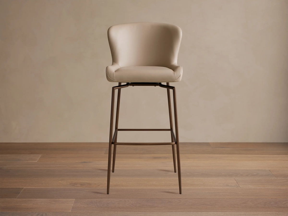 Kirsten Faux Leather Swivel Stool with beige cushioned seat and backrest, set on sleek black iron legs, wood floor background.