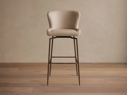 Kirsten Faux Leather Swivel Stool with beige cushioned seat and backrest, set on sleek black iron legs, wood floor background.
