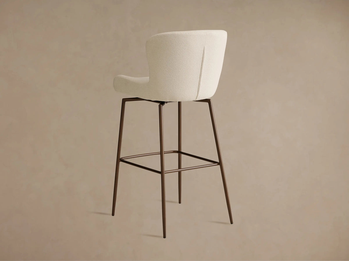 Kirsten Swivel Stool with cream upholstered seat and backrest, black iron legs, and footrest, on a wooden floor.