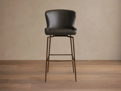 Kirsten Faux Leather Swivel Stool with sleek black seat, curved backrest, and slender powder-coated iron legs on a wooden floor.