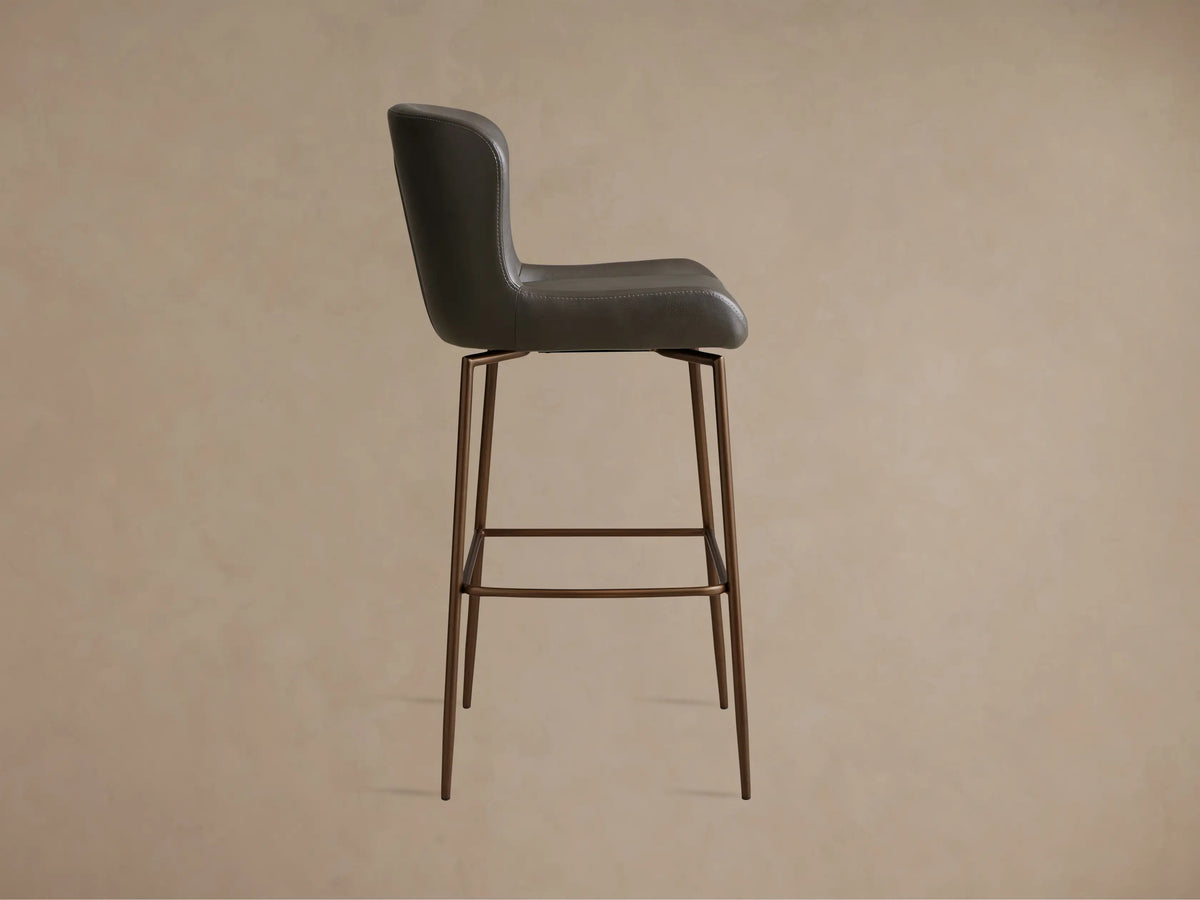 Kirsten Faux Leather Swivel Stool with a dark brown seat, curved back, and bronze metal legs. The stool features visible stitching.