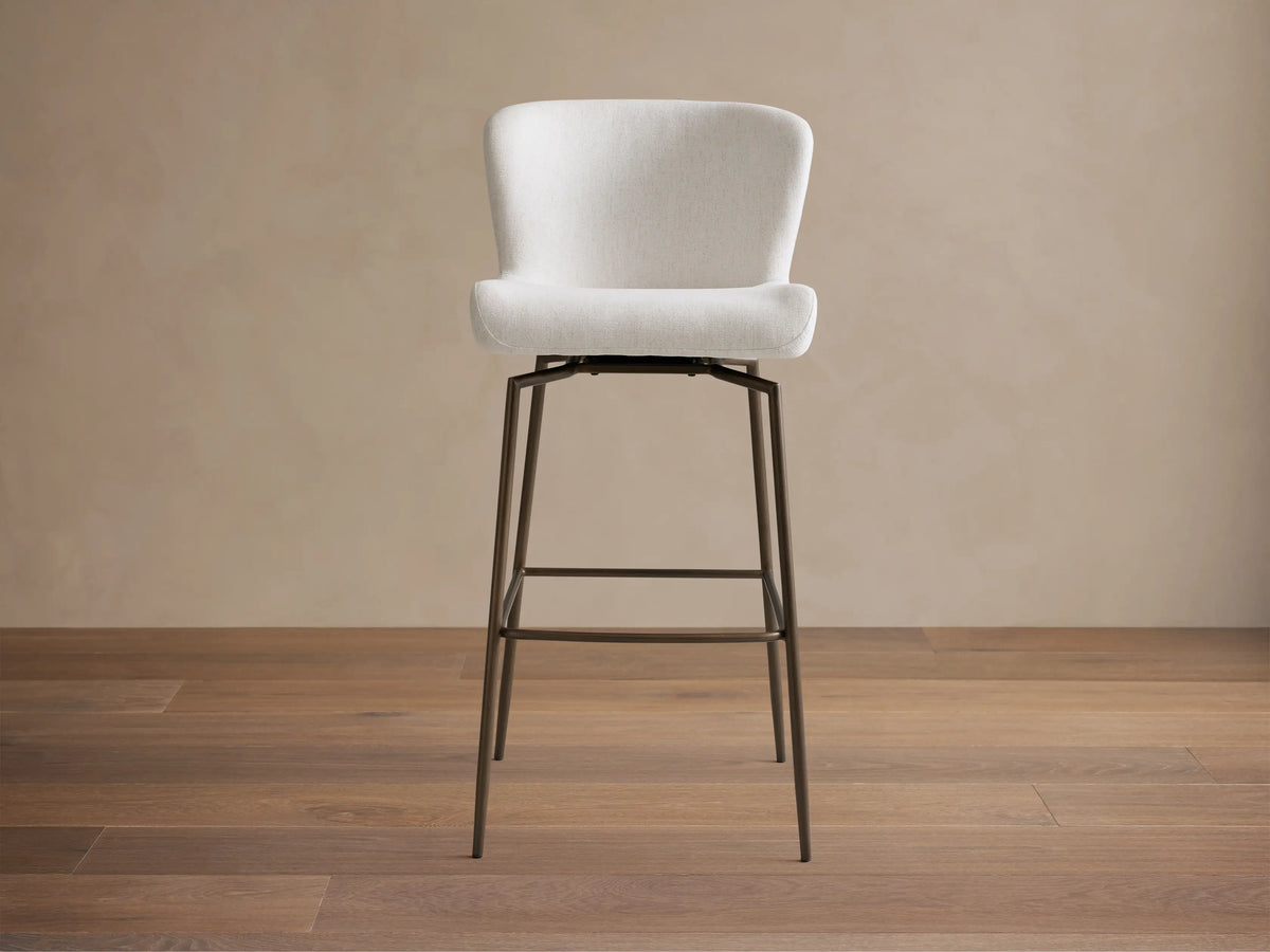 Kirsten Swivel Stool with a plush, white curved seat and black powder-coated iron legs on a wooden floor, side view.