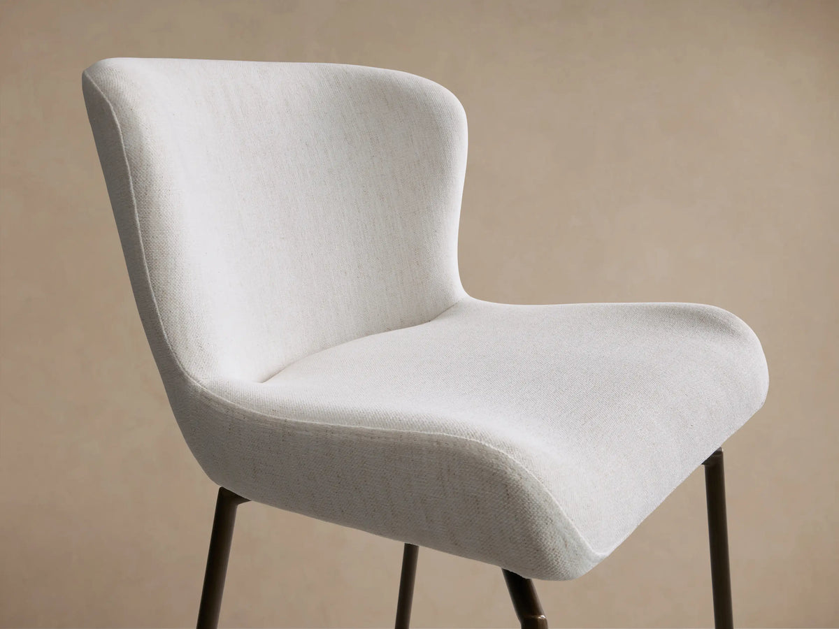 Kirsten Swivel Stool with a cream upholstered seat and backrest, black powder-coated iron legs, and a footrest on a wooden floor background.
