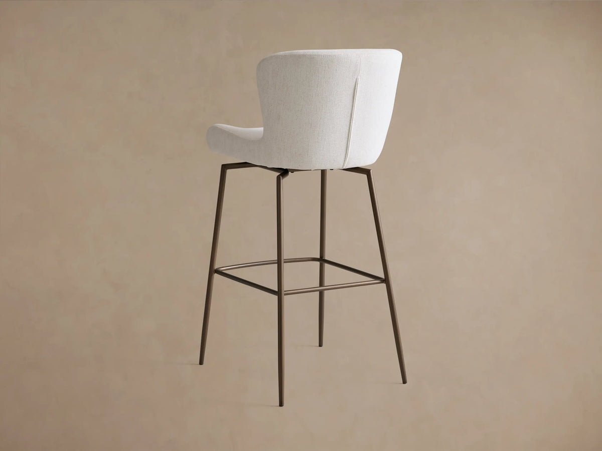 Kirsten Swivel Stool with curved, cushioned backrest and seat in light gray fabric, on dark powder-coated iron legs.