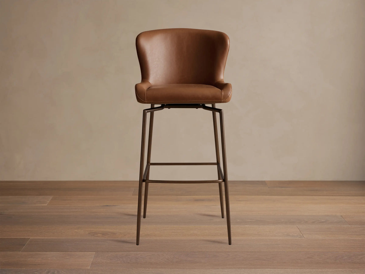 Kirsten Faux Leather Swivel Stool with a brown seat and backrest, iron legs, and a 360-degree swivel mechanism on a wooden floor.