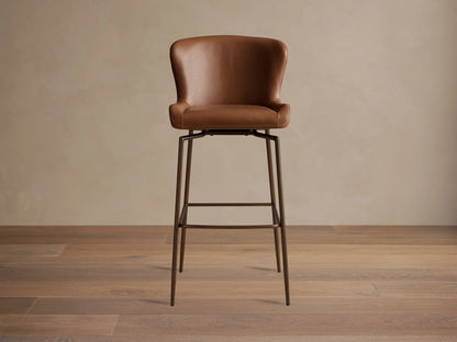 Kirsten Faux Leather Swivel Stool with a brown seat and backrest, iron legs, and a 360-degree swivel mechanism on a wooden floor.