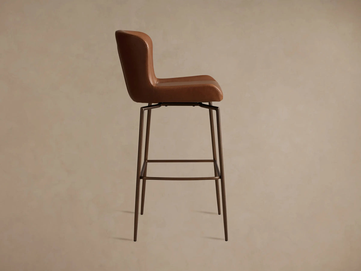 Brown Kirsten Faux Leather Swivel Stool seat close-up, showing smooth faux leather texture with visible stitching, and slender metal legs.