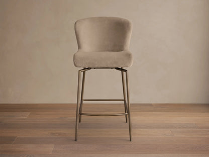 Front view of a light beige upholstered Kirsten Swivel Stool with a curved back and bronze metal legs and footrest.