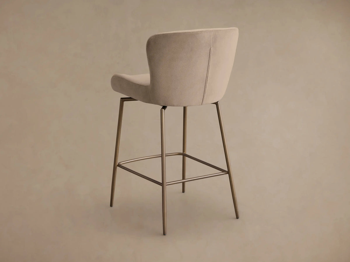Close-up of the beige Kirsten Swivel Stool, highlighting the curved upholstered seat and backrest, with visible stitching and bronze iron frame.