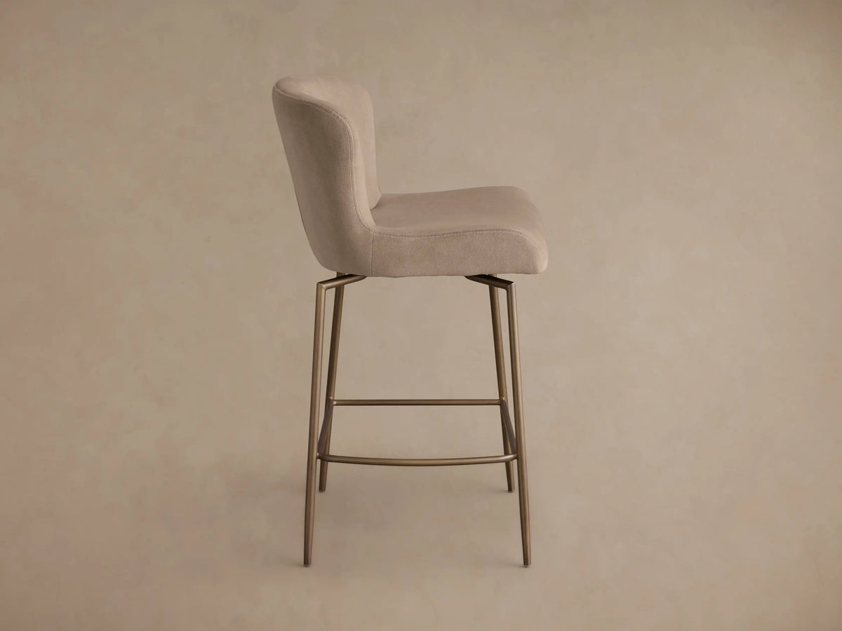 Rear view of the beige Kirsten Swivel Stool with a curved upholstered back and seat, supported by powder-coated bronze metal legs.