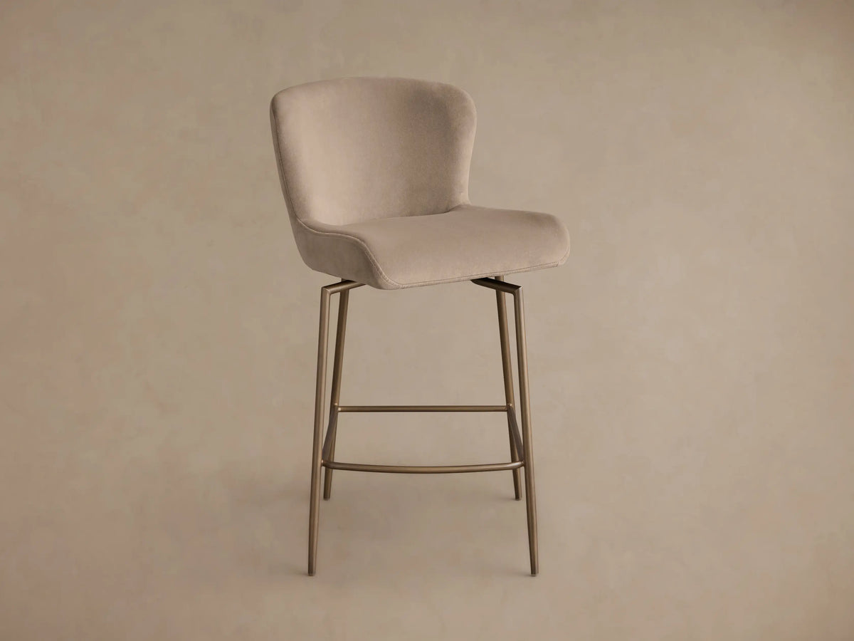 Side profile of a beige upholstered Kirsten Swivel Stool with a bronze-toned metal frame and angled legs.