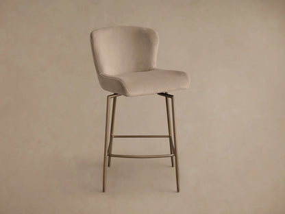 Side profile of a beige upholstered Kirsten Swivel Stool with a bronze-toned metal frame and angled legs.