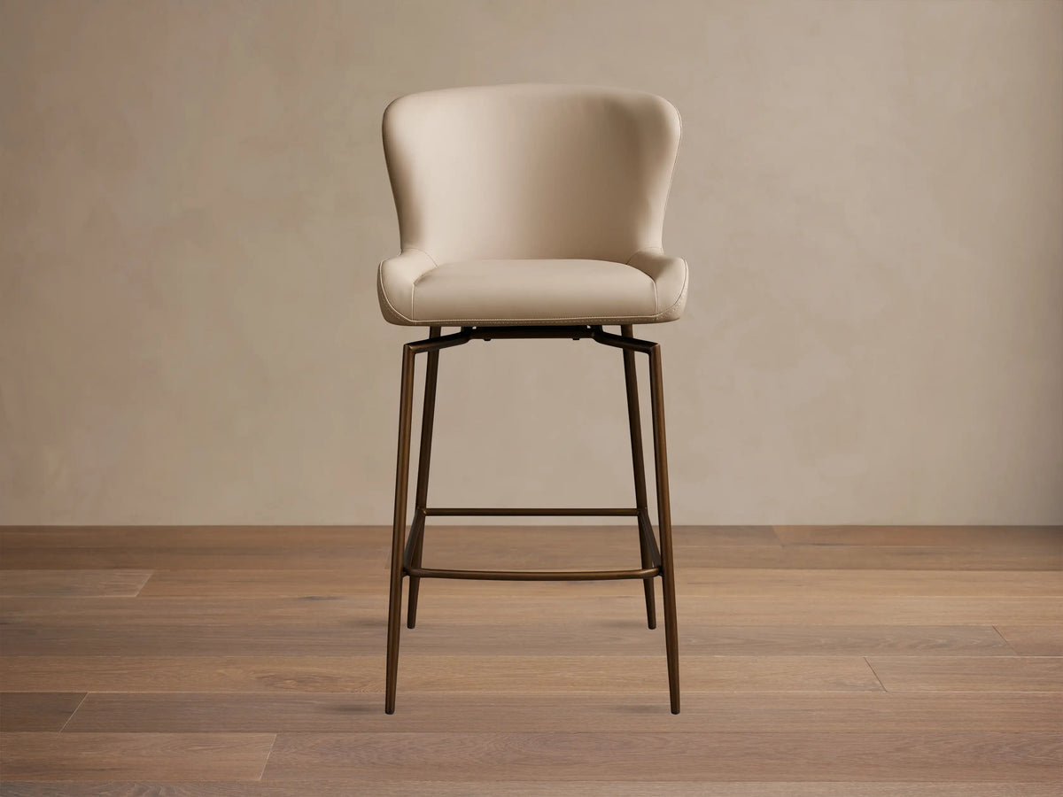 Kirsten Faux Leather Swivel Stool with beige cushioned seat and back, on sleek powder-coated black iron legs, on wooden floor.