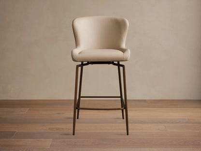 Kirsten Faux Leather Swivel Stool with beige cushioned seat and back, on sleek powder-coated black iron legs, on wooden floor.