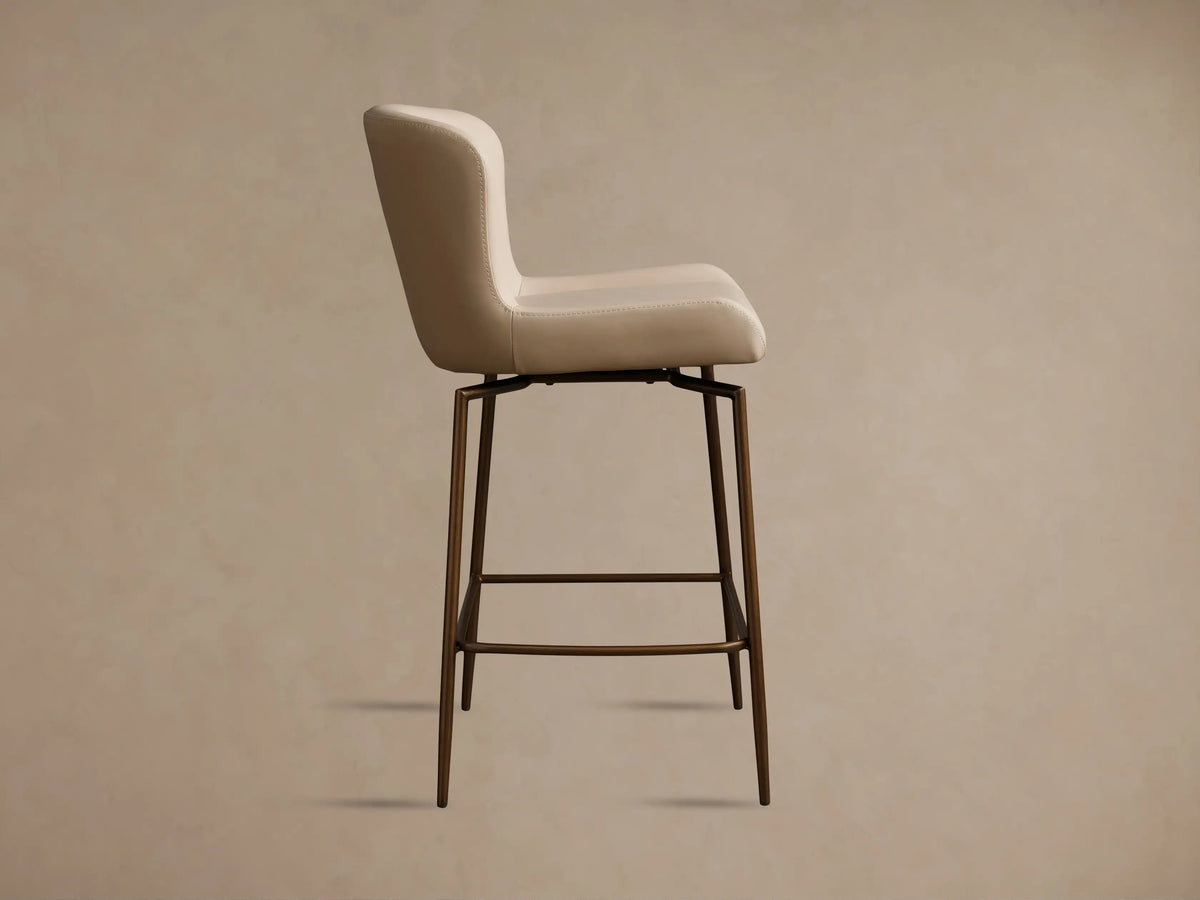 Kirsten Faux Leather Swivel Stool with a curved backrest in light beige, resting on slender, powder-coated iron legs.