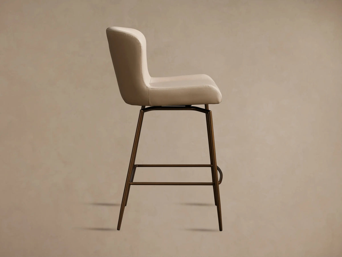 Kirsten Faux Leather Swivel Stool with a beige seat and backrest, bronze powder-coated iron legs, shown from the side profile.