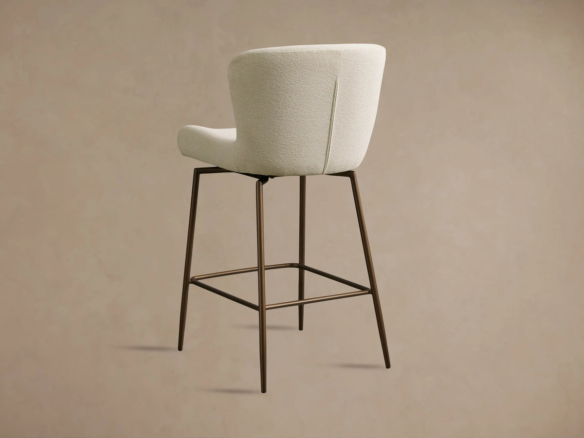 Kirsten Swivel Stool with light textured fabric upholstery, showcasing curved backrest and seat on slender metal legs.