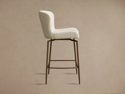 Kirsten Swivel Stool in side view; cream cushioned seat and backrest on powder-coated iron legs with footrest, on a beige background.