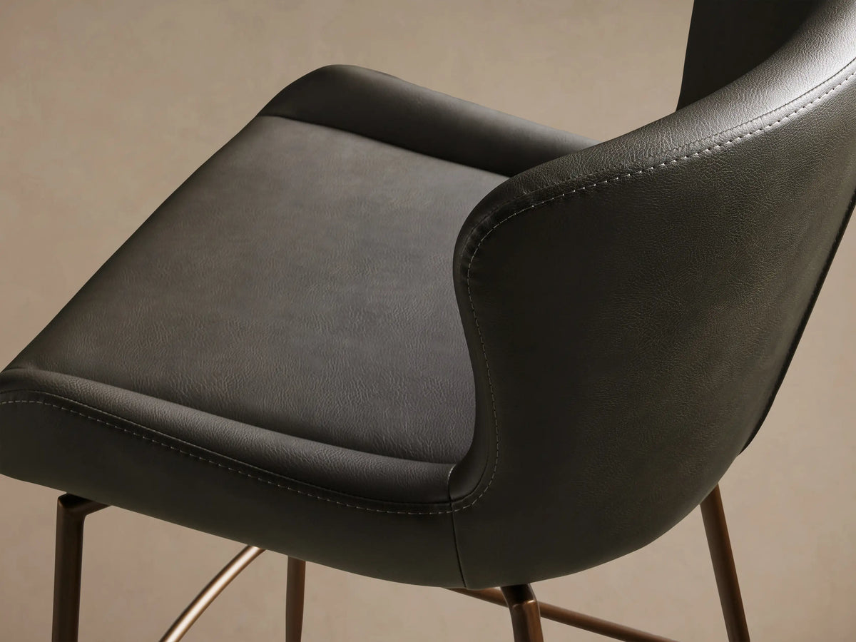 Kirsten Faux Leather Swivel Stool with black curved seat and backrest, on bronze powder-coated iron legs, on light wood floor.