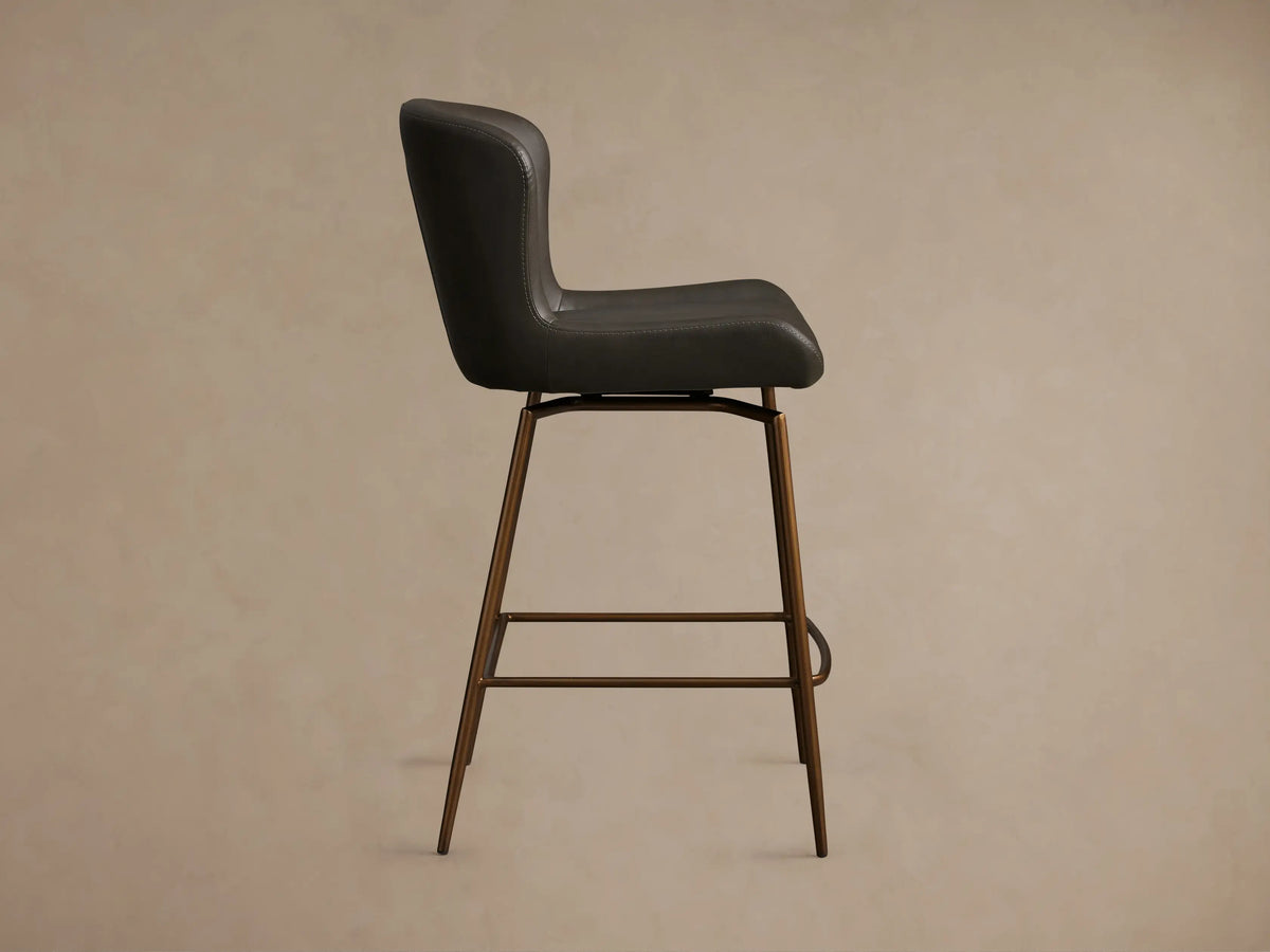 Kirsten Faux Leather Swivel Stool with dark upholstery, side view. Bronze powder-coated iron legs, foam seat with backrest.