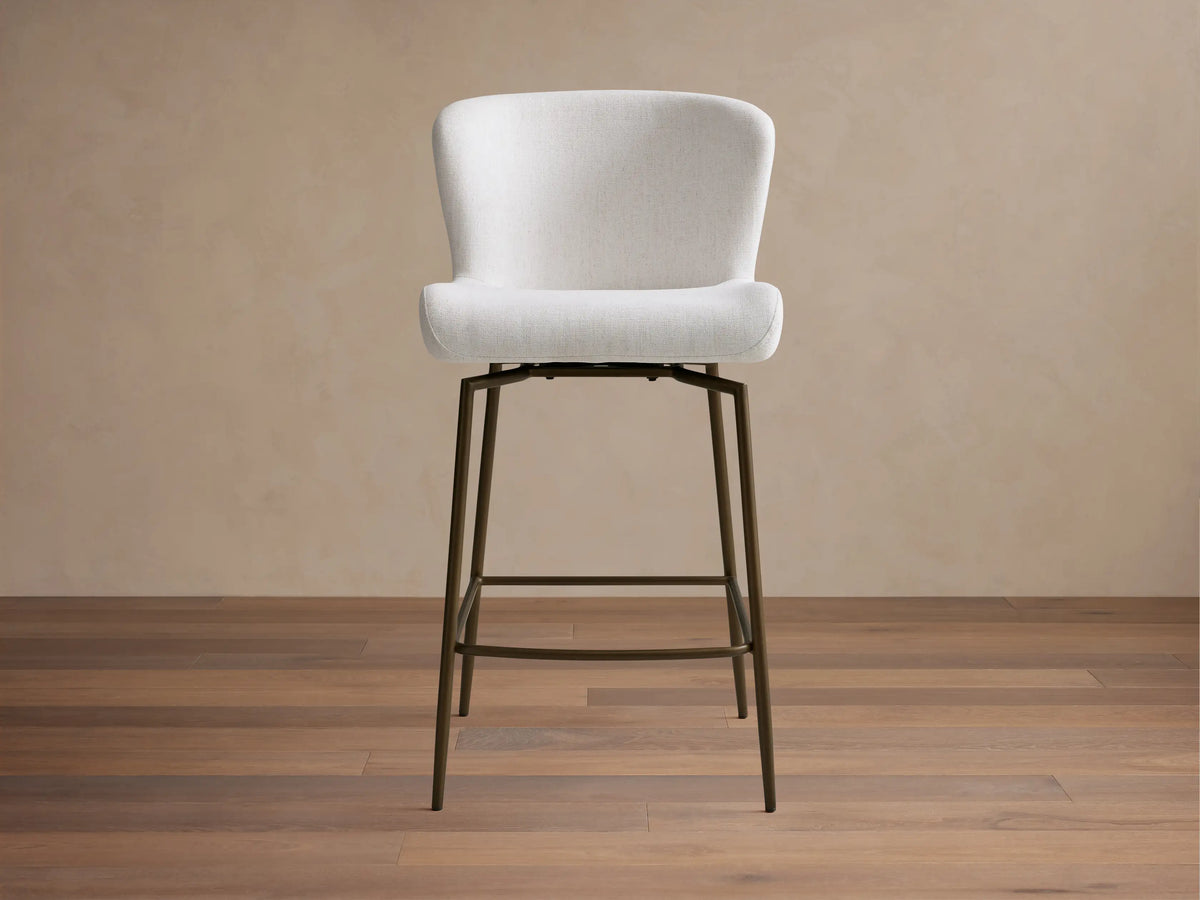 Kirsten Swivel Stool with white cushioned seat, curved backrest, and black powder-coated iron frame on wooden floor.