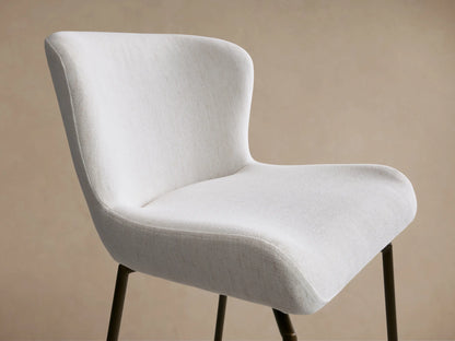 Kirsten Swivel Stool with a white cushioned seat and back, iron frame, and legs. Set on a wooden floor with a beige background.