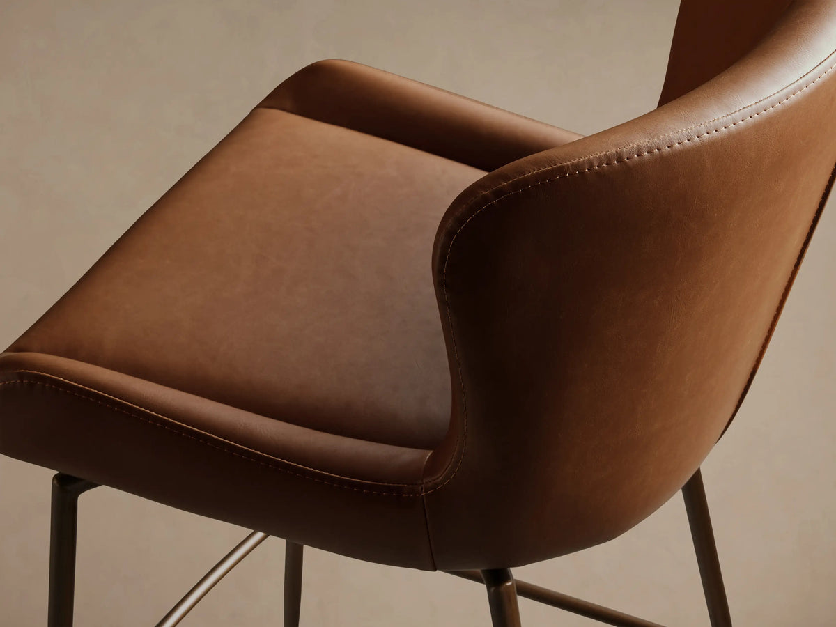 Kirsten Faux Leather Swivel Stool with brown seat and backrest on tall black metal legs on a wooden floor.