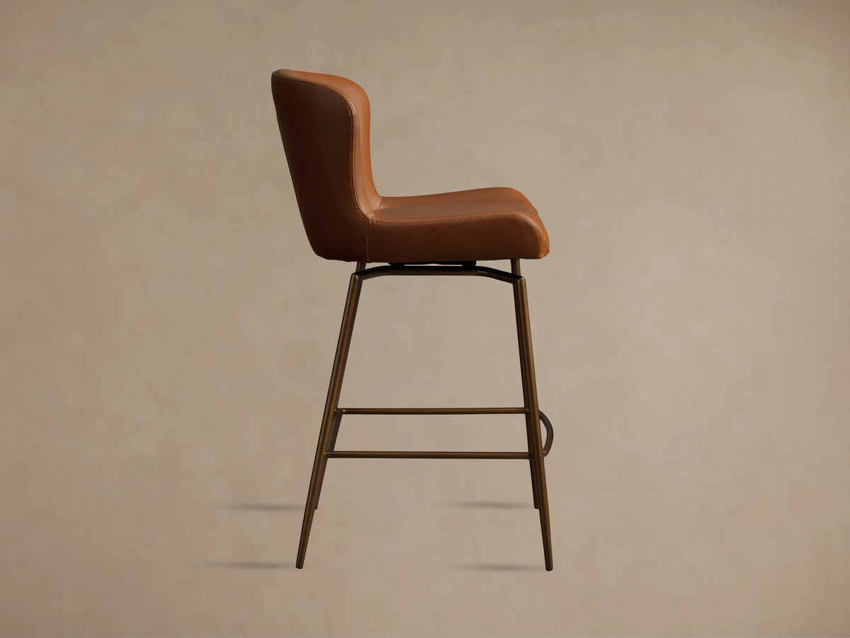 Kirsten Faux Leather Swivel Stool with brown seat and curved backrest on black iron legs, shown on wood floor.