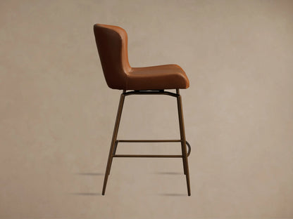 Kirsten Faux Leather Swivel Stool with brown seat and curved backrest on black iron legs, shown on wood floor.